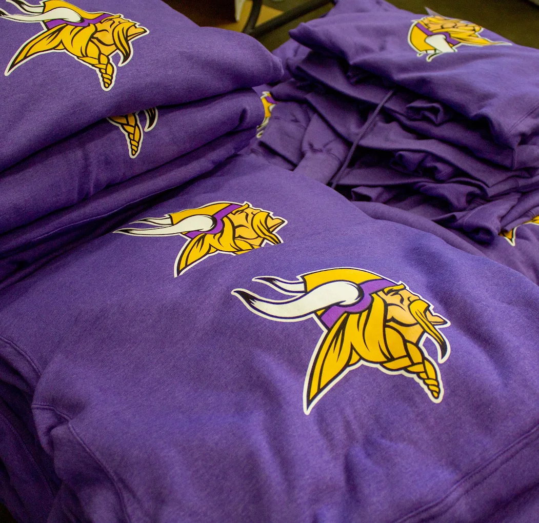 Stacked purple hoodies with yellow team logo prints
